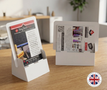 Load image into Gallery viewer, Two white cardboard display stands holding printed brochures and cards, placed on a wooden tabletop in a softly blurred indoor setting. A circular 'Made in the UK' badge appears in the bottom right corner.