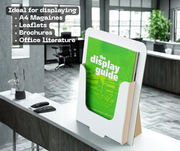 A white  cardboard display guide holder for with a A4 Mangazine standing on a white counter in a modern office setting, holding a green booklet. Text on the top left reads 'Ideal for displaying A4 Magazines, Leaflets, Brochures, Office Literature'.